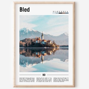 Può includere: Una stampa incorniciata con una vista panoramica del lago di Bled in Slovenia. L'immagine mostra una chiesa su un'isola, riflessa nel lago, con montagne sullo sfondo. La parola "Bled" è in alto, con "Slovenia" sopra una barra colorata.