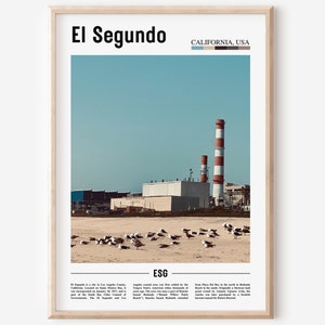 May include: A framed print featuring the text "El Segundo" and "California, USA" at the top. The image shows a coastal scene with industrial buildings, red and white smokestacks, and seagulls on the beach under a blue sky.