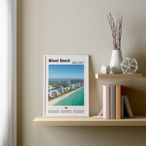 May include: A white framed poster with a black and white image of Miami Beach, Florida. The poster has the text "Miami Beach" and "Miami, Florida" in black text. The poster also has the text "MB" in black text.