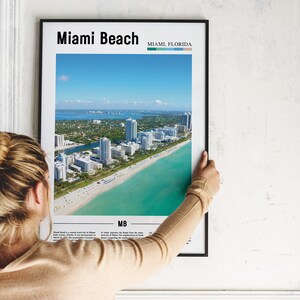 May include: A framed poster with an aerial view of Miami Beach, Florida. The poster has the text "Miami Beach" and "Miami, Florida" at the top. The poster also has the text "MB" at the bottom.