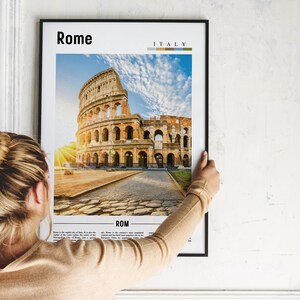 May include: A framed poster with a photograph of the Colosseum in Rome, Italy. The poster has the words "Rome" and "Italy" printed on it. The poster is being hung on a white wall.