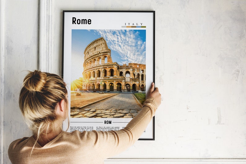May include: A framed poster with a photograph of the Colosseum in Rome, Italy. The poster has the words "Rome" and "Italy" printed on it. The poster is being hung on a white wall.