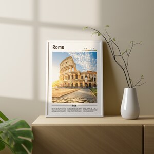 May include: A framed print of the Colosseum in Rome, Italy. The image shows the ancient amphitheater with a bright blue sky and white clouds. The text "Rome" and "Italy" are printed at the top of the frame, and the text "ROM" is printed at the bottom.
