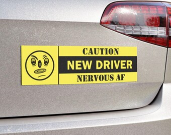 May include: A yellow rectangular car magnet with the text "CAUTION NEW DRIVER NERVOUS AF" in black. The magnet also features a cartoon face with a worried expression. The magnet is attached to the back of a silver car.