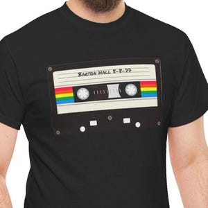 May include: Black t-shirt featuring a graphic of a cassette tape with a rainbow stripe and the text "Barton Hall 5-8-77". The cassette tape design includes details like the tape reels and the tape label.