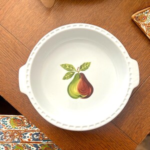 May include: White ceramic pie dish with a pear illustration. The dish has a scalloped edge and two handles. The pear is green and red with green leaves.