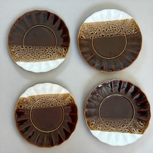 Puede incluir: Cuatro platos de cerámica con borde festoneado. Los platos presentan un centro marrón oscuro, una banda beige texturizada y una sección blanca. Los platos están dispuestos en un patrón cuadrado sobre un fondo neutro.