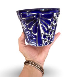 May include: A ceramic flower pot featuring a white base with hand-painted deep blue floral and geometric patterns. The design includes large petal motifs and grid-like details around the exterior surface of the tapered vessel.