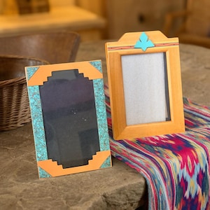 May include: Two wooden picture frames with Southwestern designs. One frame has turquoise accents and orange corners. The other frame has a turquoise leaf design at the top. Both frames are empty.