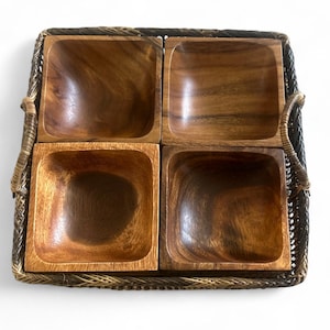 Pode incluir: Uma bandeja quadrada com quatro tigelas de madeira. As tigelas são de cor castanha quente e têm cantos arredondados. A bandeja é feita de material tecido em tons de castanho e bege, com alças nas laterais.