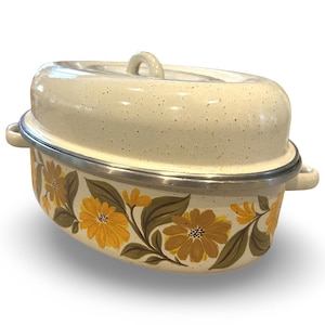 May include: Cream-colored enamelware casserole dish with a lid. The dish features a floral design with yellow flowers and green leaves. It has a silver rim and handles. The lid has a loop handle.