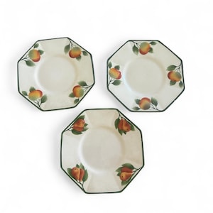 Pode incluir: Três pratos octogonais com fundo creme. Cada prato tem uma borda verde e é decorado com maçãs pintadas e folhas verdes. As maçãs são vermelhas, laranja e amarelas.