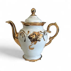 May include: A white porcelain teapot with gold accents. The teapot features a gold handle, spout, and lid. Gold leaf designs adorn the body of the teapot. The teapot is a classic design.