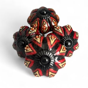 以下が含まれることがあります： 花柄のデザインが施された、4つの装飾的なキャビネットノブ。ノブは、赤と金のアクセントが付いた黒いベースが特徴です。各ノブは黒い中心部と光沢のある仕上げが施されています。ノブは白い背景に対して円形に配置されています。