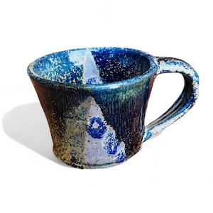 May include: A handcrafted ceramic mug with a distinctive, textured pattern. The mug showcases a dark blue glaze with lighter blue and white highlights, and a robust handle. The exterior has a rough, organic texture, ideal for enjoying tea or coffee.