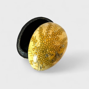 May include: An egg-shaped decorative box with a hinged lid. The box is painted with a yellow background and a design of yellow flowers and a butterfly. The interior of the box is black.