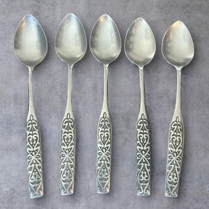 May include: Five silver spoons with ornate, engraved handles. The spoons have a classic design with oval bowls and detailed floral patterns on the handles. The spoons are arranged in a row against a gray background.