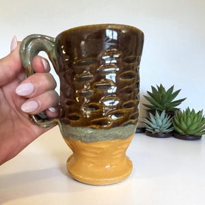 Peut inclure: Mug en céramique fait à la main avec une partie supérieure marron texturée et une base jaune. La poignée est vert-gris. Le mug est conçu avec un motif unique et convient aux boissons chaudes ou froides.