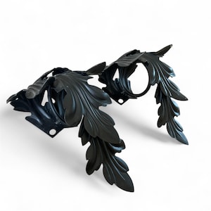 Puede incluir: Diseño decorativo de hojas de metal negro. La metalurgia presenta formas detalladas de hojas y un elemento circular. La pieza es probablemente un elemento decorativo para muebles o diseño de interiores.