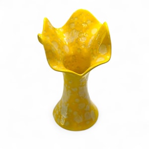 Könnte beinhalten: Eine gelbe Keramikvase mit gerüschtem Oberteil. Die Vase hat ein gesprenkeltes Muster aus Weiß und Gelb. Die Vase ist ein dekorativer Gegenstand, der sich zum Ausstellen von Blumen oder als eigenständiges Kunstwerk eignet.