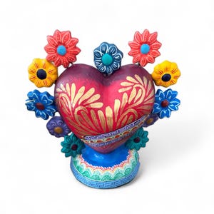 May include: A handcrafted, heart-shaped decorative piece with a deep red base and gold floral accents. The heart is surrounded by colorful, stylized flowers in red, blue, and yellow. The base is blue with a decorative border.