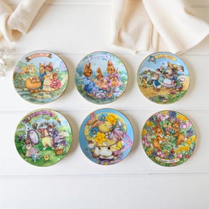 Puede incluir: Seis platos decorativos de Pascua con bordes dorados. Cada plato presenta una ilustración colorida diferente de conejos y otros animales con temática de Pascua. Los platos son redondos y tienen el año impreso.