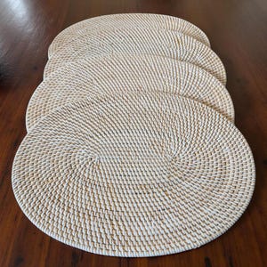 Puede incluir: Cuatro manteles individuales redondos y tejidos de color beige claro están dispuestos sobre una superficie de madera marrón oscuro. Los manteles individuales tienen un diseño en espiral en el centro y una superficie texturizada.