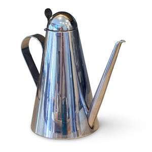 May include: A polished stainless steel oil pourer with a conical body, a curved handle, and a long, slender spout. The lid has a small, round handle. The oil pourer reflects the surrounding environment.