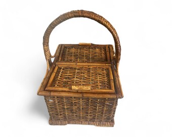 May include: A brown wicker picnic basket with a curved handle and two hinged lids. The basket has a rectangular shape with a woven design and a sturdy base. The handle is also made of woven wicker.