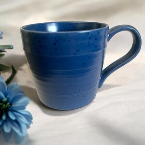 May include: A blue ceramic mug with a curved handle. The mug has a speckled finish and horizontal etched lines around the body. The mug is a solid blue colour.