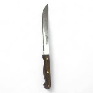 May include: A steak knife with a serrated stainless steel blade and a dark brown wooden handle. The handle is secured with three brass rivets. The knife is designed for cutting meat.