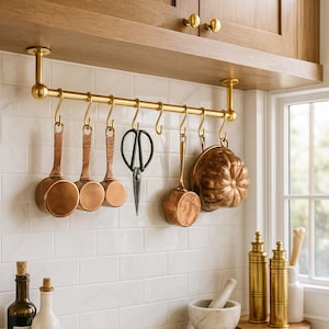 Peut inclure: Intérieur de cuisine avec ustensiles de cuisine en cuivre suspendus à une barre en laiton. Comprend des louches en cuivre, un moule décoratif et des ciseaux noirs. Bouteilles et mortier et pilon sur le comptoir blanc.