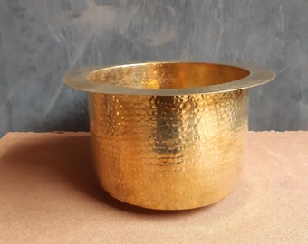 May include: A large, round, hammered brass planter with a wide rim. The planter is gold in color and has a textured surface.