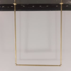 Peut inclure: Une barre de suspension en métal doré avec deux supports verticaux et une barre horizontale. La barre est fixée à un plafond noir.