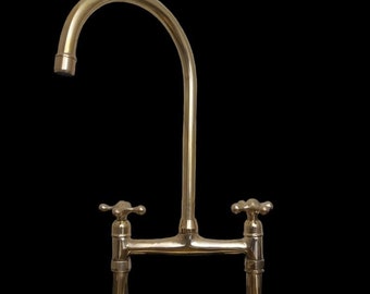 May include: A polished brass kitchen faucet with a high arc spout and two cross-handle controls.