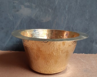 May include: A hammered gold metal bowl with a wide rim. The bowl has a textured surface and is sitting on a brown surface.