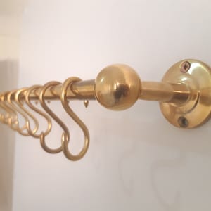 May include: A gold-toned metal wall-mounted coat rack with a round finial and multiple hooks.