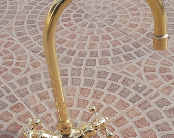 May include: A gold-toned kitchen faucet with a high arc spout and two lever handles. The faucet is mounted on a tiled surface.