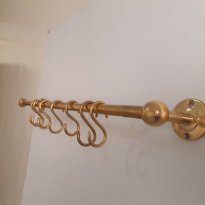 May include: A gold metal kitchen utensil rack with a round knob and a wall mount. The rack has six hooks for hanging kitchen utensils.
