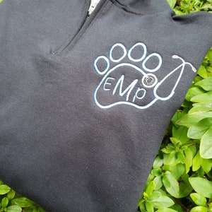 May include: Black zippered sweatshirt with a white paw print embroidered on the front. The paw print has the letters "EMO" inside and a stethoscope is next to it.