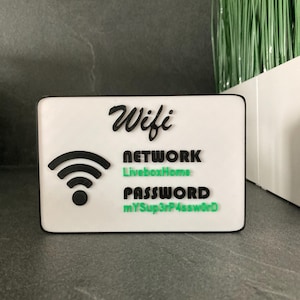 Peut inclure: Panneau rectangulaire blanc avec texte noir et vert indiquant "Wifi", "Network LiveboxHome" et "Password mYSup3rP4ssw0rD". Un symbole wifi noir est également présent. Le panneau a une bordure noire.