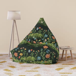 Puede incluir: Un puf verde oscuro con un estampado floral con flores coloridas y follaje verde. El puf está en una habitación con una lámpara blanca y una pequeña mesa auxiliar. La alfombra tiene un patrón crema y amarillo.