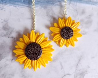 Pode incluir: Dois colares de corrente dourada com pingentes de girassol amarelo. Os girassóis têm centros castanhos.