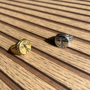 May include: Two rings with a silver and gold finish. The rings feature a raised design of a person with arms outstretched.