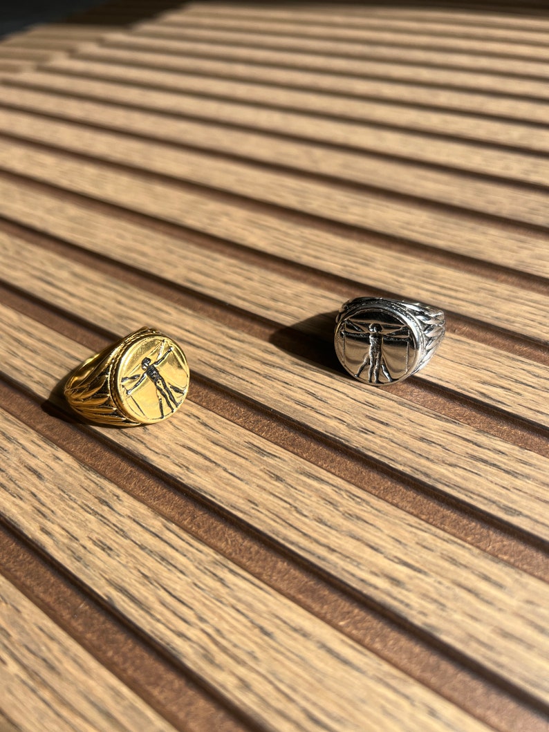May include: Two rings with a silver and gold finish. The rings feature a raised design of a person with arms outstretched.