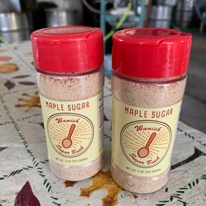 May include: Two clear plastic jars with red lids containing maple sugar. The jars have yellow labels with the text "Maple Sugar", "Wanish Sugar Bush", and "Net Wt. 4 oz (113 grams)".