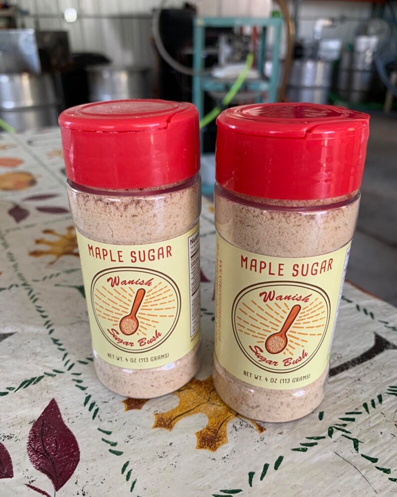 May include: Two clear plastic jars with red lids containing maple sugar. The jars have yellow labels with the text "Maple Sugar", "Wanish Sugar Bush", and "Net Wt. 4 oz (113 grams)".
