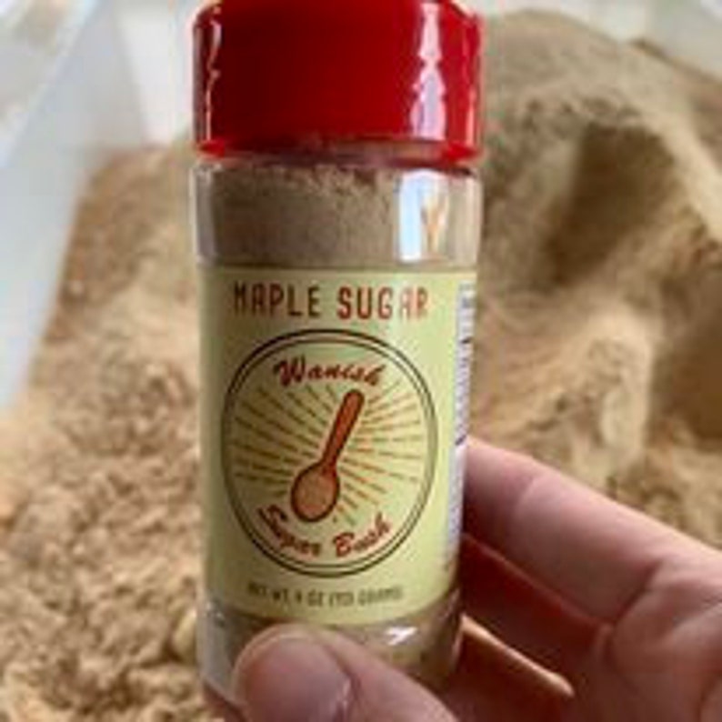 May include: A small, clear plastic jar with a red lid filled with a light brown powder. The jar has a yellow label with the text "Maple Sugar" and "Wanish Super Bush" in black lettering. The jar is 4 oz (113 g).