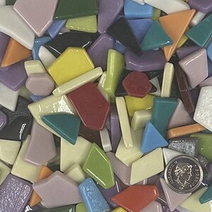 May include: A close-up of a collection of colorful mosaic tiles in various shapes and sizes. The tiles are in shades of pink, green, yellow, blue, orange, and purple. A US quarter is included for size reference.
