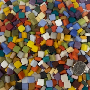 May include: A collection of small, square mosaic tiles in a variety of colors, including red, orange, yellow, green, blue, and white. A US quarter is included for size reference. These tiles are likely used for crafting or decorative purposes.